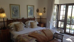 Une chambre à coucher avec un grand lit, deux tables de chevet avec des lampes, un banc en bois et une vue sur l’extérieur par une grande fenêtre.