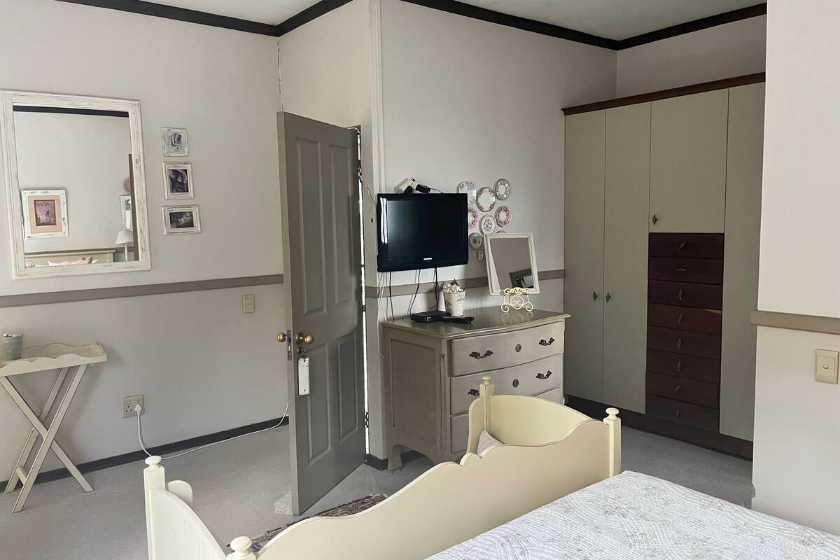Un dormitorio con cama, cómoda, televisor, puerta y espejo.