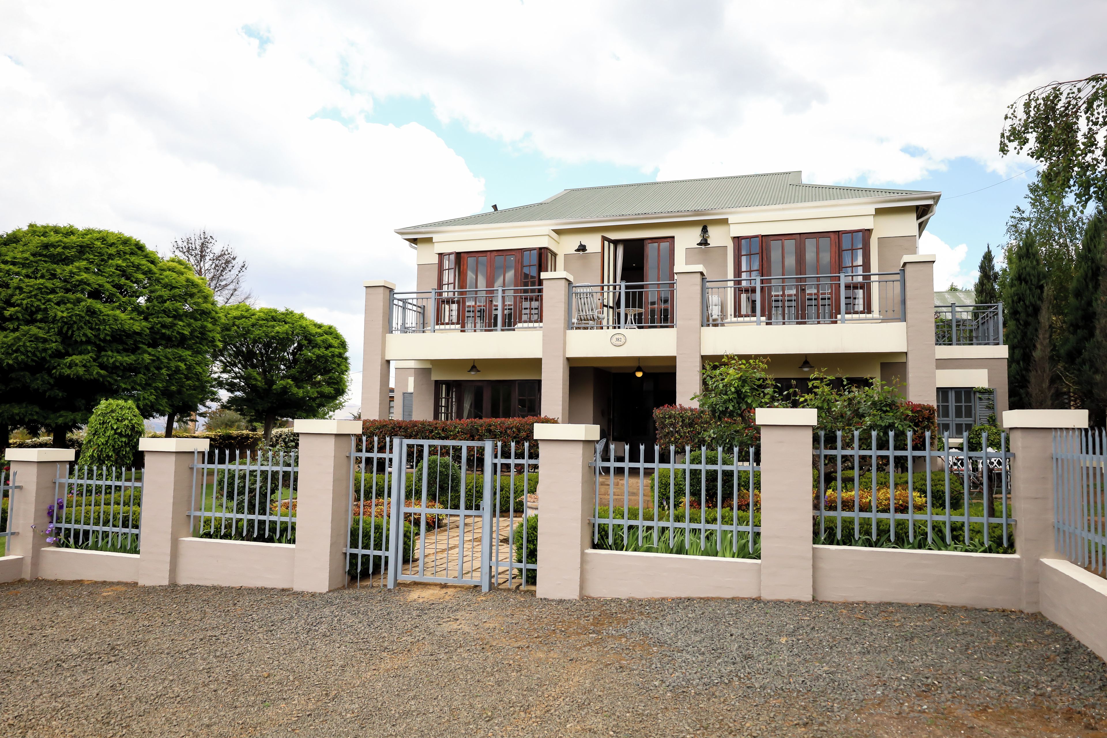 A two-story building with a gated entrance, a balcony on the upper floor, and a well-maintained garden.