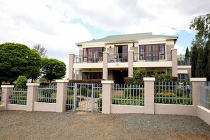 A two-story building with a gated entrance, a balcony on the upper floor, and a well-maintained garden.