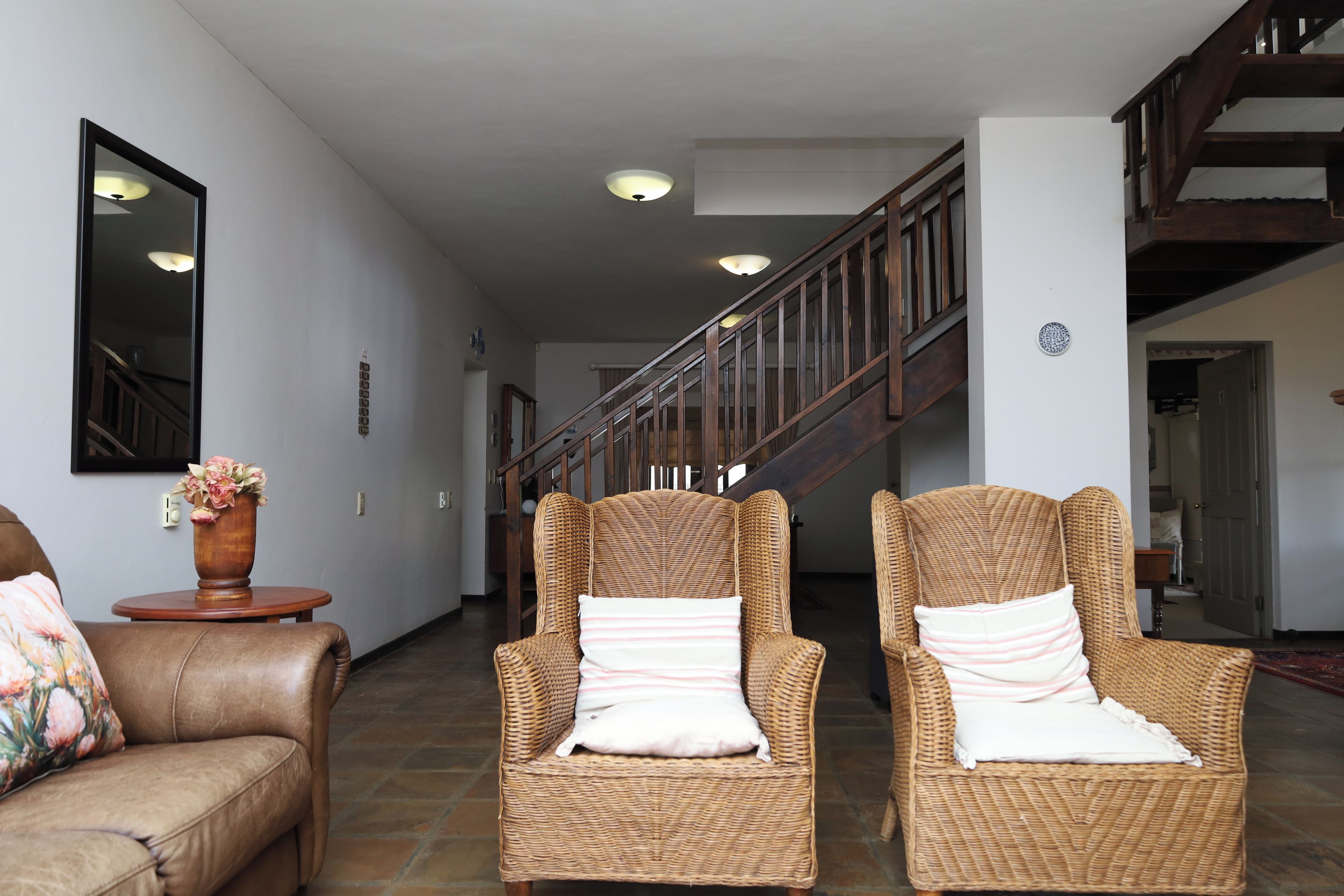 A hallway with two wicker armchairs, a brown leather sofa, and a wooden staircase.
