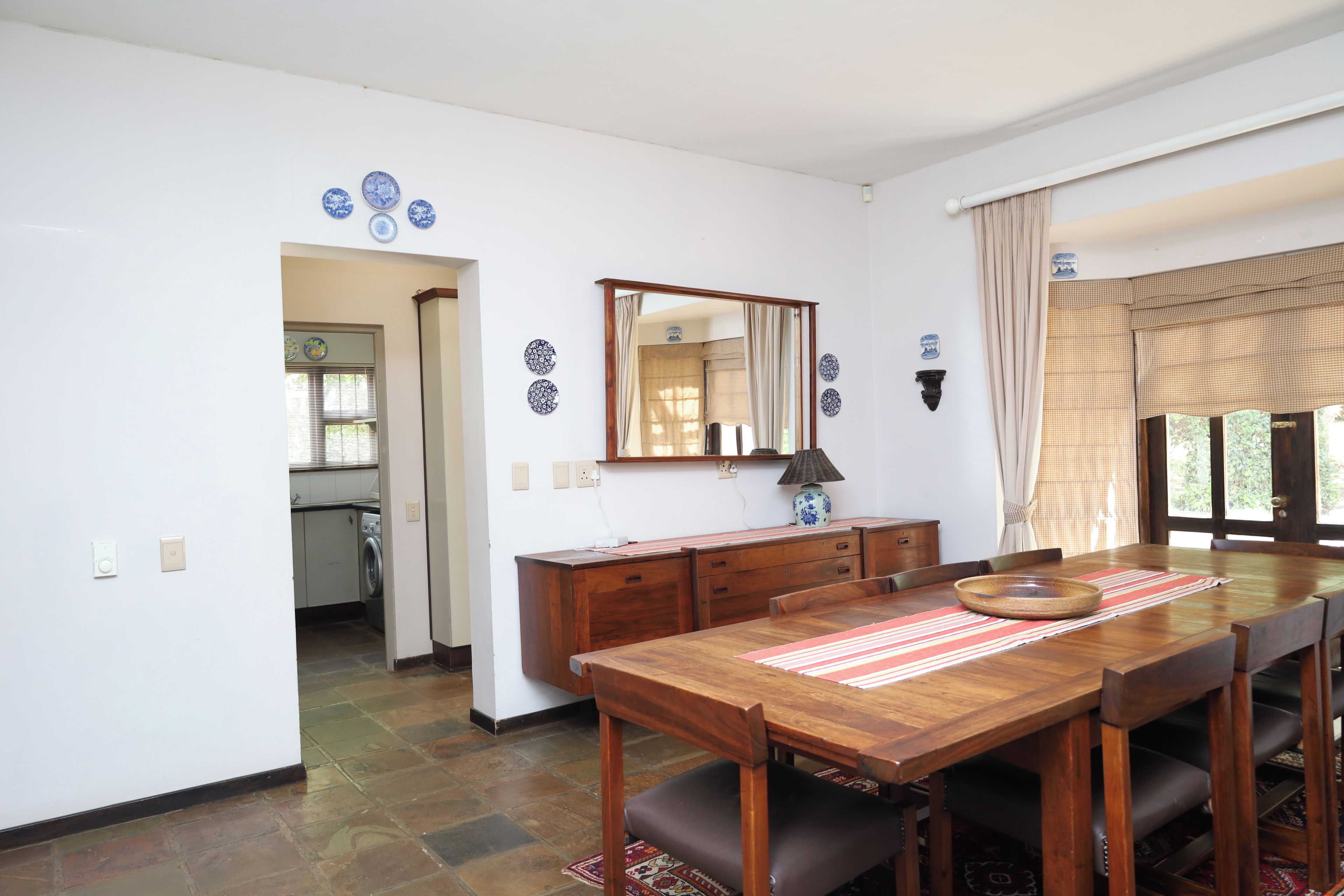 A dining area with a wooden table, chairs, a mirror, and a view of a kitchen.