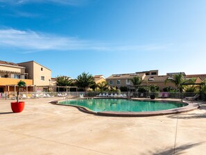 Una piscina con sillones de descanso, una planta en maceta roja y edificios al fondo.