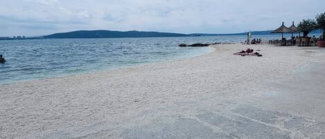 A beach with a rocky shoreline, a few people relaxing, and a distant view of hills.