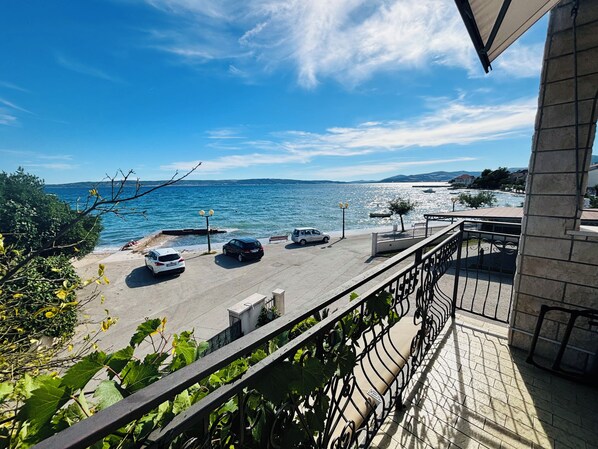 Un balcon avec vue sur la mer, des voitures garées et un bâtiment en pierre.