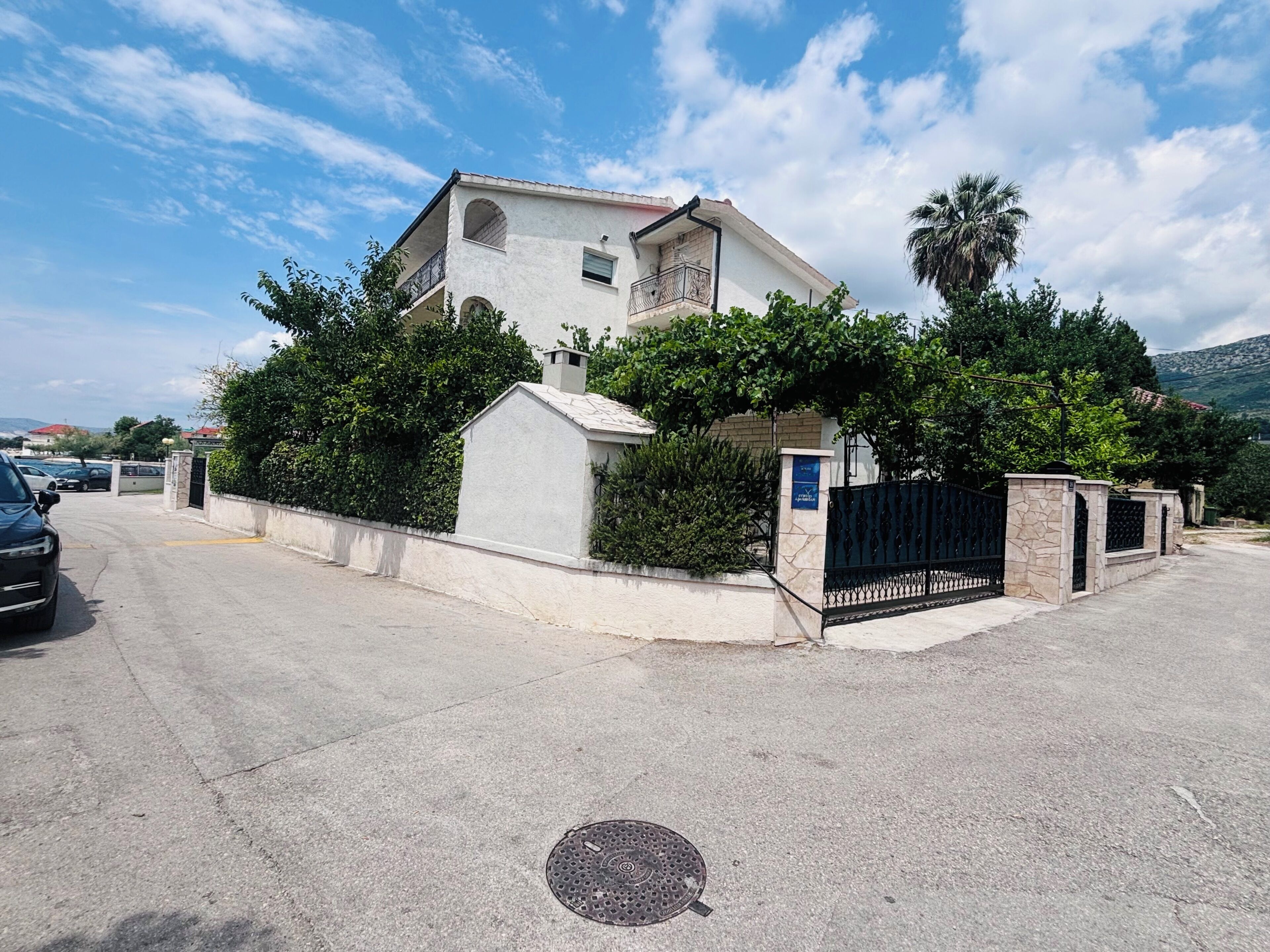 A two-story building with a gated entrance, a manhole cover on the ground, and a clear sky.