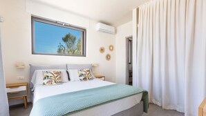 Um quarto com uma cama, janela, ar condicionado, mesa de cabeceira e porta.