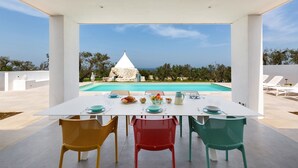 Uma área de refeições com uma mesa posta para dois, com vista para uma piscina e para o mar.