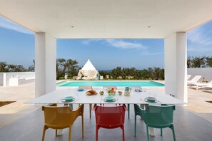 Ein Essbereich mit einem für zwei Personen gedecktem Tisch, mit Blick auf einen Pool und das Meer.