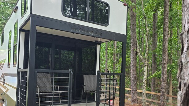 A camper with a covered deck, a ladder, and a picnic table.