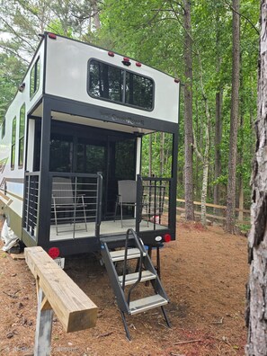 A camper with a covered deck, a ladder, and a picnic table.