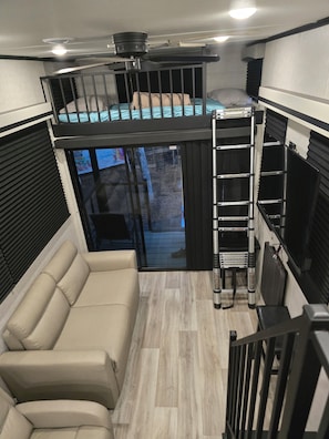 A compact interior with a bunk bed, a sofa, and a ladder.