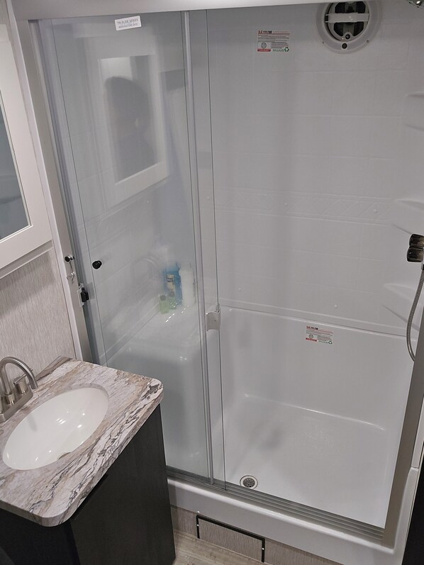 Un baño con ducha envuelta en vidrio, un lavabo con encimera de mármol y un espejo sobre el lavabo.