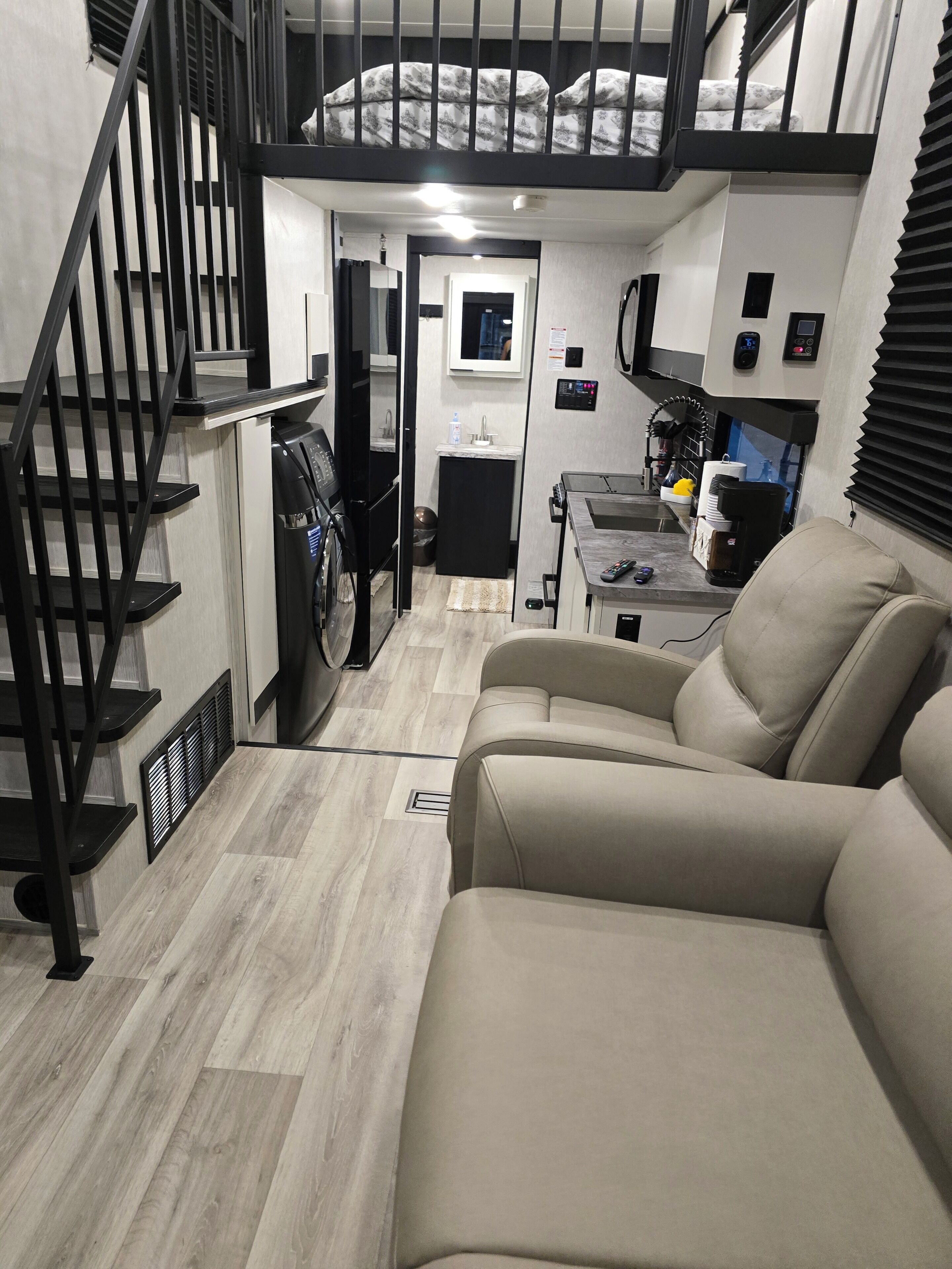 A compact living space with a sofa, a staircase, a kitchenette, and a small bathroom.
