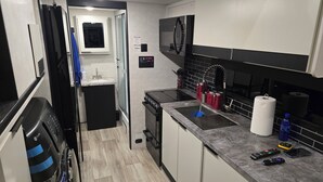 A modern kitchen with a built-in microwave, a gas stove, a sink, and a countertop with a paper towel holder and a water bottle.