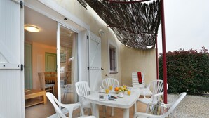 Eine Terrasse mit Tisch und Stühlen, eine Tür zu einem Innenraum sowie ein Hecken im Hintergrund.