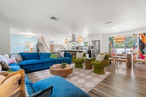 A modern living room with a blue sofa, green armchairs, a wooden coffee table, and a kitchen in the background. - Fun & Sun! Heated Pool, Pickleball, Mini Golf, Game Room + More! Sleeps 18! (Seminole)