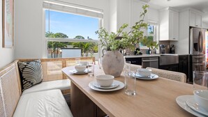 Eine moderne Küche mit weißen Schränken, Edelstahlgeräten und einem Essbereich mit Holztisch und weißen Stühlen.