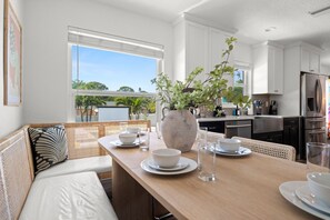 A modern kitchen with white cabinets, stainless steel appliances, and a dining area with a wooden table and white chairs. - Fun & Sun! Heated Pool, Pickleball, Mini Golf, Game Room + More! Sleeps 18! (Seminole)