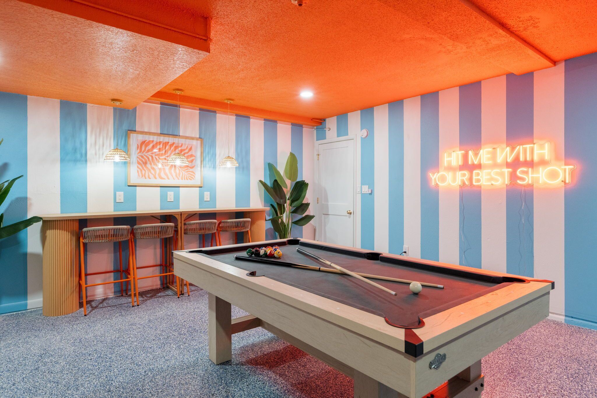 Una mesa de billar con un letrero de neón, paredes a rayas y una zona de bar.