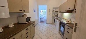 A compact kitchen with a microwave, oven, and sink. There is a dining area visible through an open door.