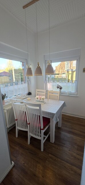 A dining area with a table, chairs, pendant lights, and a view through the window.