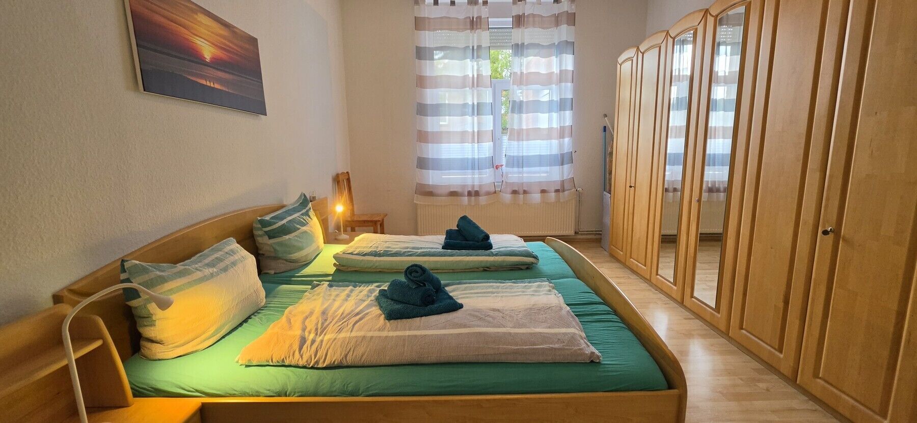 Ein Zimmer mit zwei Betten, einem Holzschrank, einem Bild an der Wand und einem Fenster mit Vorhängen.