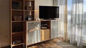 Una sala de estar con un televisor sobre un mueble de madera, cestas de mimbre y un letrero que dice 'LIEBLINGSPLAZ'.