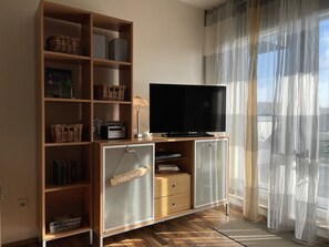 Ein Wohnzimmer mit Fernseher auf einer Holzkommode, Weidenkörben und einem Schild mit der Aufschrift 'LIEBLINGSPLAZ'.