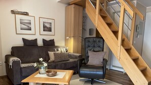 Una sala de estar con sofá, sillón, mesa de centro y una escalera de madera.