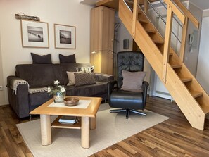 Ein Wohnzimmer mit Sofa, Sesseln, Couchtisch und einer Holztreppe.