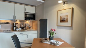 Una cocina moderna equipada con microondas, cafetera y utensilios. Hay una mesa de comedor con sillas y un florero.