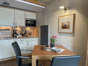 Eine moderne Küche mit Mikrowelle, Kaffeemaschine und Kochgeschirr. Ein Esstisch mit Stühlen und eine Blumenvase stehen bereit.