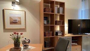 Una sala moderna con un mueble bajo para televisión de madera, un televisor de pantalla plana, una estantería, una mesa de comedor con un jarrón de tulipanes y un cuadro en la pared.