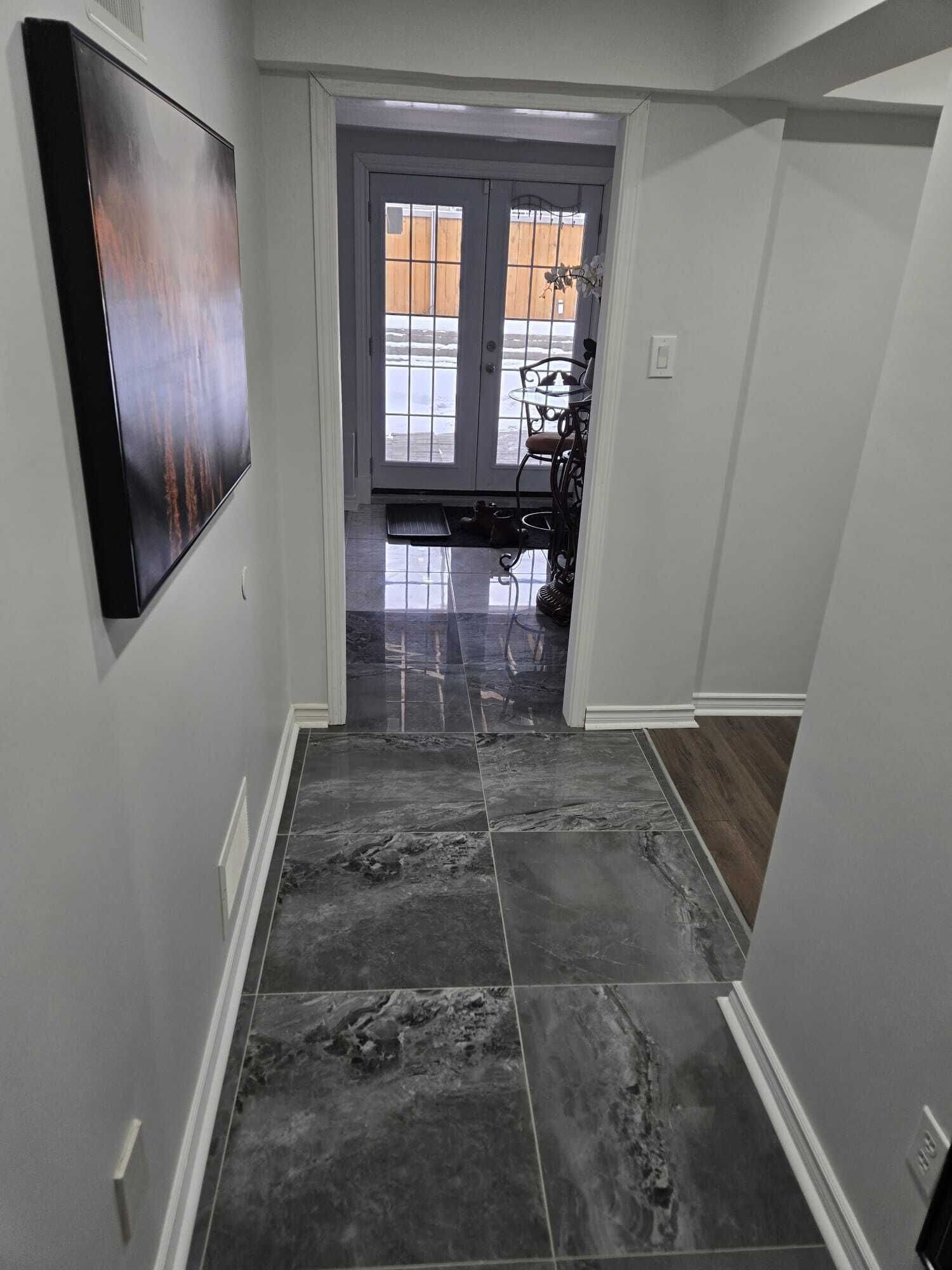 A hallway with dark marble flooring, a white door leading outside, and a small table with chairs.