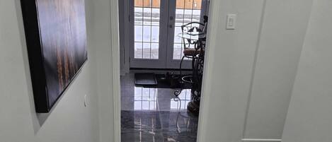 A hallway with dark marble flooring, a white door leading outside, and a small table with chairs.