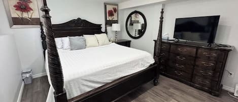 Une chambre à coucher avec un lit à baldaquin, une commode, un téléviseur et des œuvres d’art accrochées aux murs.
