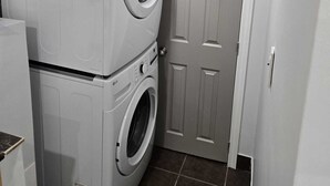 Een wasserette met gestapelde wasmachine en droger, een deur en betegelde vloer.