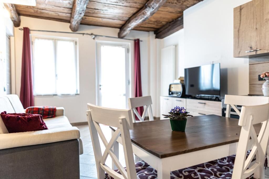 Un soggiorno moderno con divano, tavolo da pranzo, sedie, televisione e angolo cottura con pensili e piano di lavoro.
