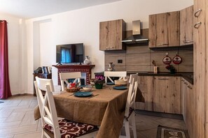 Comedor con mesa dispuesta para cuatro personas, armarios de madera, televisor y área de cocina con armarios de madera y estufa.