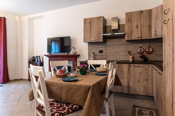 Comedor con mesa dispuesta para cuatro personas, armarios de madera, televisor y área de cocina con armarios de madera y estufa.
