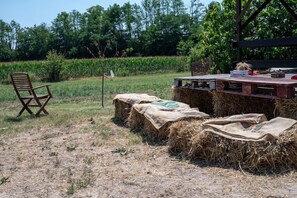 Un entorno rústico al aire libre con una mesa de madera, fardos de heno y una silla plegable.