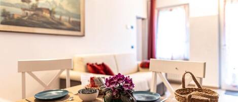 Un comedor con una mesa dispuesta para dos personas, un cuadro en la pared y vistas al exterior.