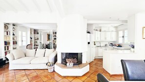 Ein Wohnzimmer mit Kamin, einer Couch und einer Küchenzeile mit weißen Schränken und Fliesenboden.