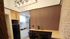 A compact kitchen with a wooden countertop, two chairs, a hanging light fixture, and a brick wall. - Hostal Andrea Gran Via (Madrid)
