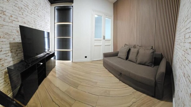 A living room with a flat-screen TV, a sofa, a wooden floor, and a white door. - Hostal Andrea Gran Via (Madrid)