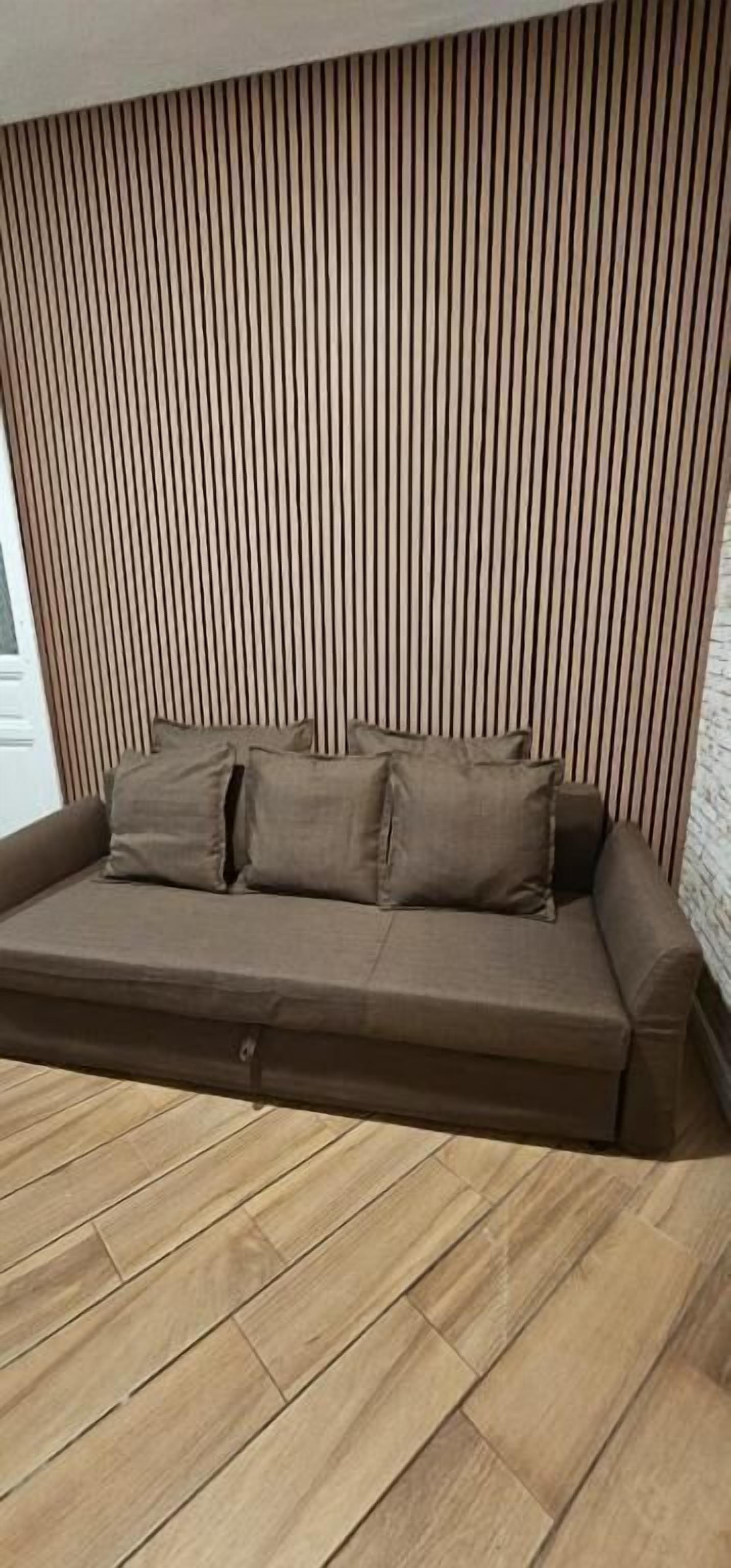 A brown sofa with cushions against a wall with vertical slats.