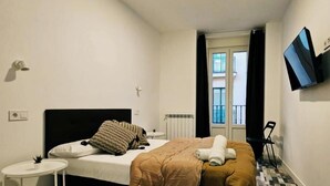 A hotel room with a bed, a small bedside table, a wall-mounted TV, and a window with curtains. - Hostal Andrea Gran Via (Madrid)