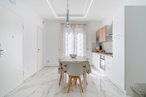 Una cocina moderna con armarios blancos, encimera de mármol y un comedor con mesa y sillas.