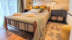 A wooden-paneled bedroom with a bed, bedside tables, and framed pictures on the wall. - Entire chalet in Kupjak (Kupjak)